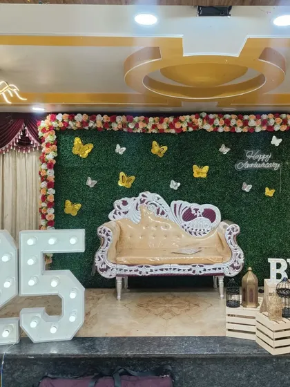 For grand milestone celebrations like a 25th anniversary, I design impressive stage setups. This features giant light-up marquee numbers, a lush green wall backdrop for photos, and an ornate sofa, turning any venue into a spectacular party space.