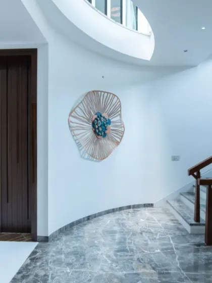 A curved wall guides the path towards a staircase in this entryway. The design uses soft curves, a mix of grey marble and white flooring, and a striking wall sculpture to create a memorable first impression.