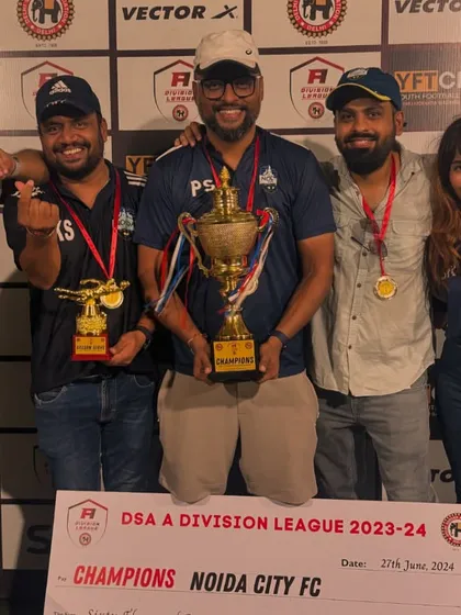 The entire management and coaching staff celebrating with the DSA A Division League trophy. This victory was a total team effort, on and off the pitch.