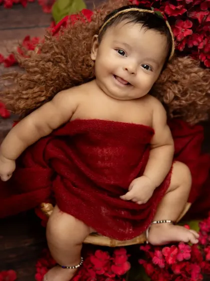 A sweet, gummy smile from a happy baby nestled in soft red wraps. The rich color and floral accents create a beautiful and warm portrait.
