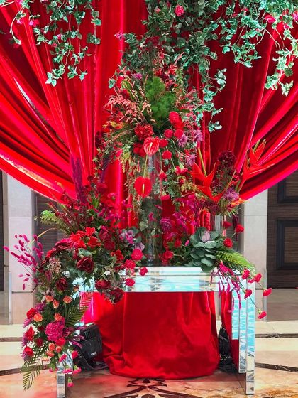 An elegant floral arrangement for a red-themed reception. A cascade of red flowers and greenery is set against a backdrop of rich red drapes, creating a stunning focal point that is both luxurious and full of life.