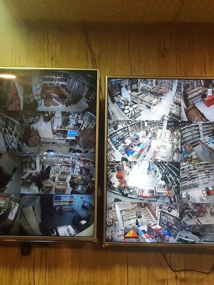 Two monitors displaying split-screen views from a comprehensive security system inside a retail store. This setup helps business owners monitor aisles, checkout counters, and storage areas simultaneously.