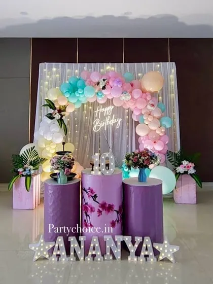 A beautiful pastel-themed birthday decoration with a light-up name display. The soft colors of the balloon arch and floral accents create a delicate and pretty setup for a girl's birthday.