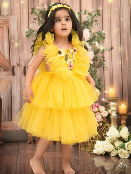 A ray of sunshine in yellow for her third birthday. This portrait captures a candid, thoughtful moment against a rustic floral backdrop.