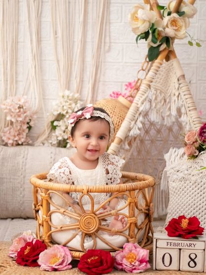 A smiling baby girl in a wicker basket, surrounded by flowers. This is a classic shot from my boho-themed sessions, full of charm and sweetness.