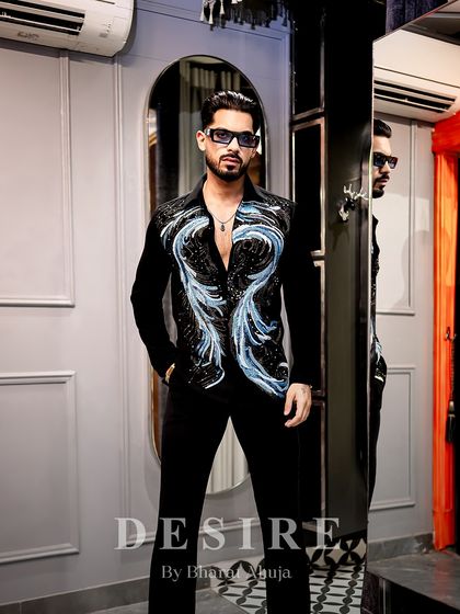 A full-length view of a statement look. The embroidered shirt paired with simple black trousers creates a balanced yet powerful ensemble that is ready for any high-end event.