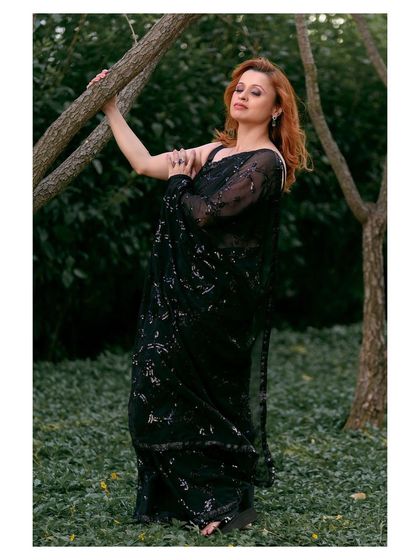 An elegant outdoor portrait in a black sequined saree. The natural setting provides a beautiful contrast to the glamorous attire.