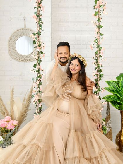 A happy couple's portrait on our floral swing. The mom-to-be is wearing a beautiful beige ruffled gown, and the shot captures a moment of pure joy and connection.
