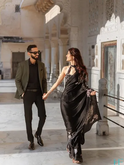 A candid walking shot through a palace corridor, capturing the effortless elegance of the couple. The movement in the bride's saree and their shared glance make this feel like a scene from a movie.