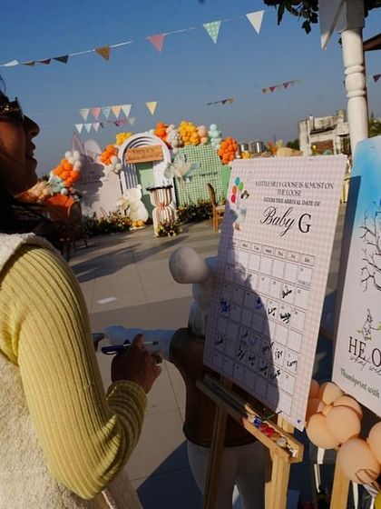 Guests participating in interactive activities, such as guessing the due date and leaving thumbprints on a 'He or She' gender reveal tree.