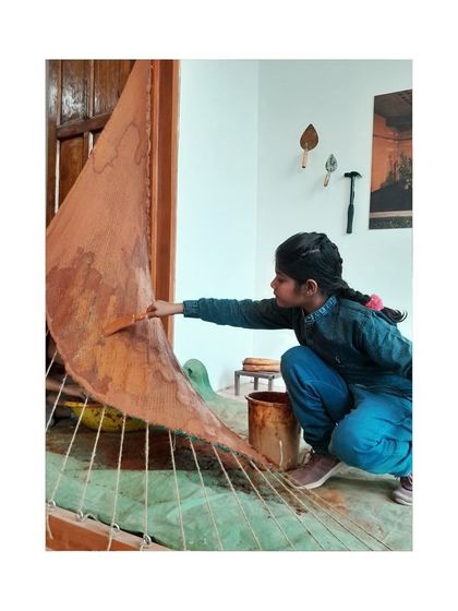 A duplicate image of a young participant applying mud to the tensile structure, fully engaged in the creative process.