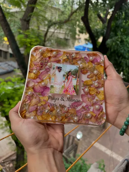 A beautiful shot of a square resin keepsake, showcasing the arrangement of pink and yellow petals, pearls, and the couple's photo. Every piece is a unique work of art.