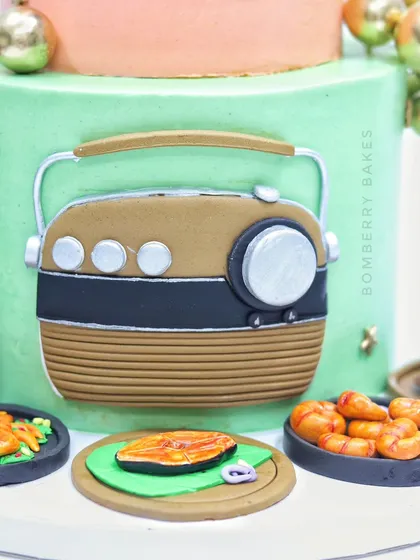 A close-up of a retirement cake for a seafood lover, featuring a vintage radio and plates of edible fried fish, prawns, and crab.