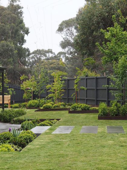 The same backyard on a rainy day, showing how the design looks beautiful in all weather. The wet stepping stones and dark fence create a moody, atmospheric scene.
