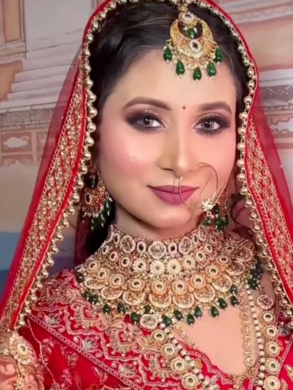 A classic red lehenga paired with a gold and green Kundan bridal set. This image shows a full bridal look with a choker, nath, and maang tikka.