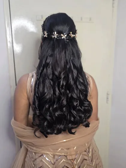 A romantic half-up, half-down hairstyle with voluminous curls and a delicate floral hair vine, created for Anjali's 'Bane Bithai' function.