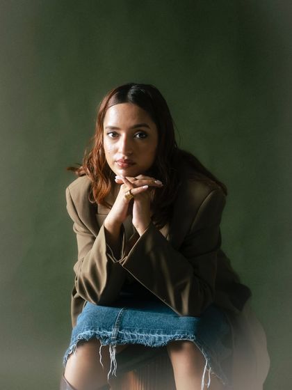 A seated portrait that combines a casual denim skirt with a formal blazer. The pose is thoughtful, and the soft, diffused lighting adds to the calm and collected mood of the shot.