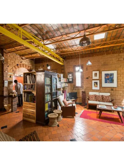 The warm and inviting living area of the Sans Souci Residence in Bengaluru, our experimental lab for ecological design. This space features exposed earth block walls, a mezzanine for spatial efficiency, and is lit naturally by skylights, eliminating the need for artificial cooling.