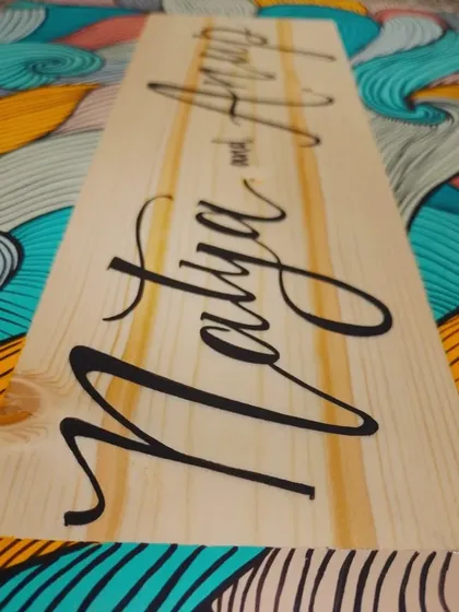 A close-up perspective of the "Natya and Anup" plaque, focusing on the elegant calligraphy and the natural beauty of the pine wood.