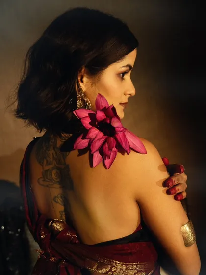 A beautiful detail shot, with a lotus flower placed on the model's shoulder. The image is soft, sensual, and focuses on the textures of skin, fabric, and flower.