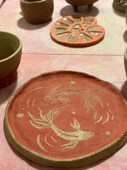 A beautiful, raw terracotta plate with a sgraffito design of two koi fish. The carving reveals the lighter clay underneath, creating a stunning contrast.
