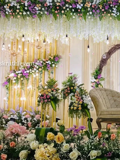 An exceptionally lush and elegant reception stage. The decor is filled with a variety of pastel flowers, hanging wisteria, and sparkling chandeliers, creating a luxurious and enchanting setting.