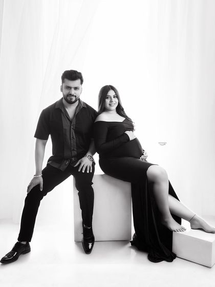 A stylish black and white couple portrait. The seated pose and coordinated black outfits create a chic and modern look against the bright studio background.
