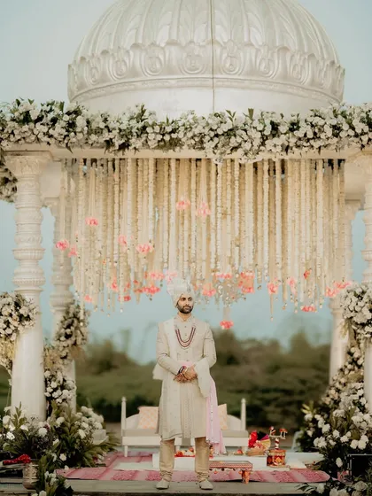 The groom, waiting patiently at the mandap. This portrait captures his regal presence under the stunning floral canopy, a moment of calm before he is joined by his bride.