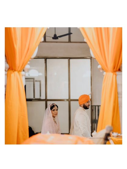 A beautifully framed shot of Suraj and Kajal during their ceremony, seen through the vibrant orange drapes of the Gurudwara.