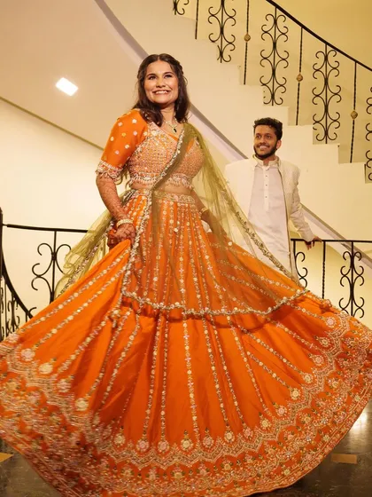 A fun, twirling shot of the bride in a vibrant orange lehenga for her engagement, showing how the makeup and hair hold up beautifully in motion.