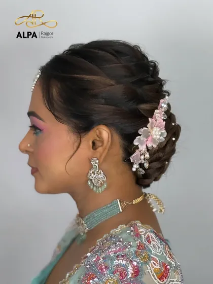 An elegant bun hairstyle featuring a delicate, handmade pink floral hair accessory with pearls, perfect for a reception or cocktail party.