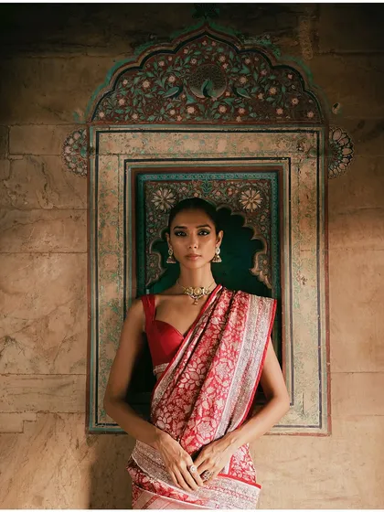 A model wears a red Banarasi saree for the Anita Dongre 'Crafts of India' campaign. The styling is classic and elegant, letting the intricate weave of the textile be the hero.