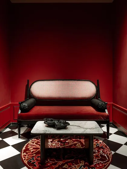 A bold statement from our House of Goya collection. This waiting nook is drenched in a fiery red, creating a dramatic and memorable experience. The classic caned settee and checkerboard floor add a touch of vintage glamour.