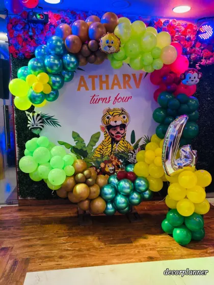 Four-ever wild and free! This photo showcases the main backdrop for a jungle-themed 4th birthday, featuring a custom print of the birthday boy and a colorful balloon garland with a large '4' foil balloon.