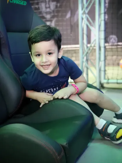 A young boy gives a happy smile while sitting in a large gaming chair at an arcade.