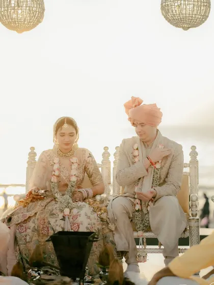 The couple sits at their beachside ceremony, the soft, hazy light of the setting sun creating a dreamy and romantic atmosphere.