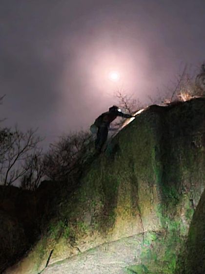 A climber reaches the top of a boulder under the glow of the moon. These are the quiet, powerful moments that make night climbing so special.
