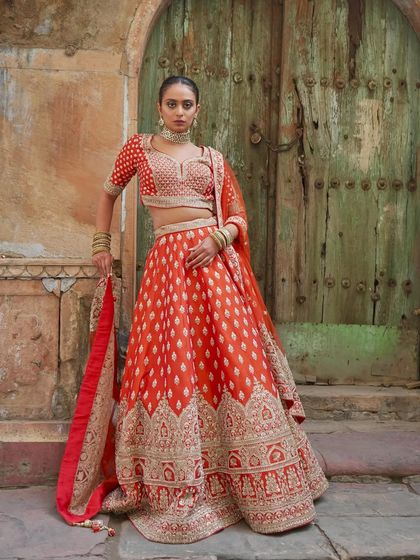 A Maharani-inspired look. This orange-red lehenga with its unique buti work and a heavily embroidered border is a perfect blend of tradition and modern bridal style.