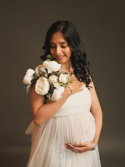 Holding a bouquet of white peonies, she looks down with a soft smile. This minimalist portrait combines the beauty of nature with the elegance of a studio setting.