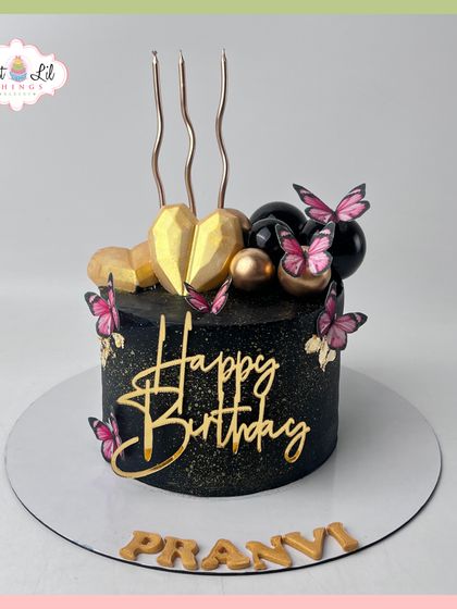 A bold and glamorous black and gold birthday cake. This design features a geometric heart, fluttering butterflies, and a dramatic color scheme for a truly striking look.