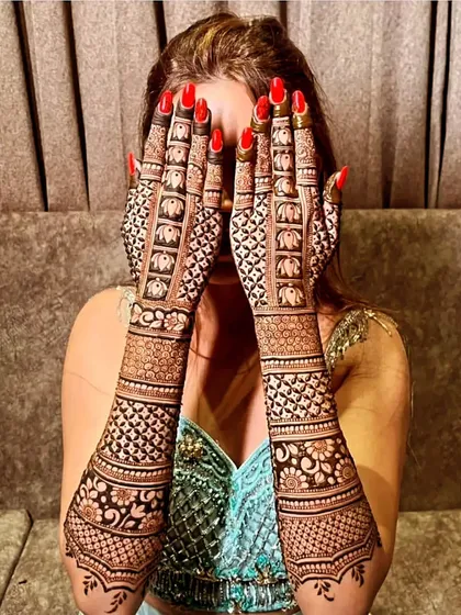 A classic bridal pose, with the hands covering the face to show off the intricate elephant and jaali patterns.