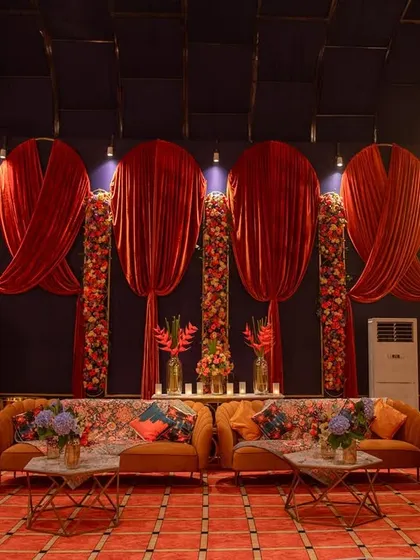 A comfortable and stylish lounge area for guests to relax between games. The decor features plush sofas, vibrant cushions, and dramatic red velvet drapes against a deep blue wall.