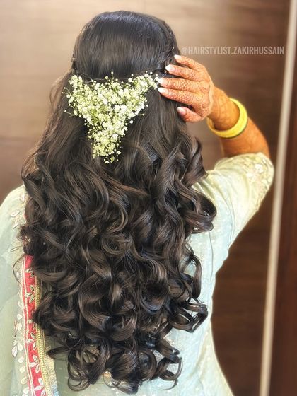 A romantic half-up hairstyle with a braided crown and a heart-shaped arrangement of baby's breath. The soft curls complete this lovely look, perfect for an engagement or pre-wedding shoot.