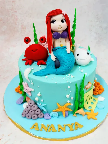 This enchanting mermaid cake features Ariel sitting with her friends Sebastian the crab and Flounder, surrounded by a vibrant coral reef.