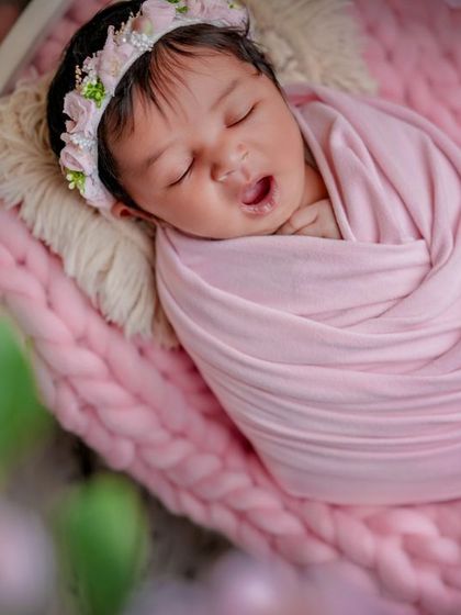 A sleepy little rosebud. This close-up shot captures a tiny yawn from a baby swaddled in pink, nestled on a miniature floral bed.