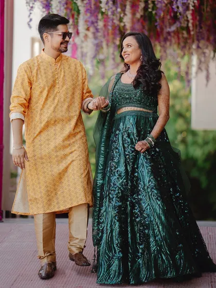 The couple walks hand-in-hand at their pre-wedding event. Their coordinated yellow and green outfits look vibrant against the floral decor.
