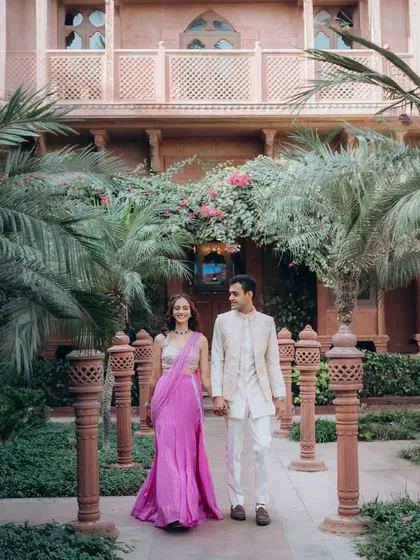 A classic walking shot of Kanav and Saloni in the courtyard of the Welcomhotel Khimsar. The symmetry of the architecture and the lush greenery create a regal and romantic setting.