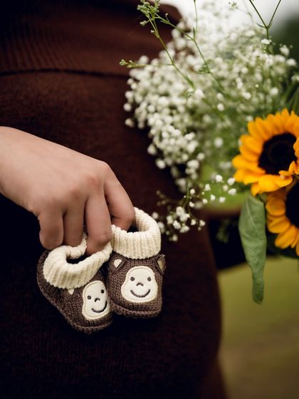 A close up on the details: tiny, cute monkey-themed baby shoes held against the backdrop of a sunflower bouquet. It’s a sweet and gentle way to hint at the little one on the way.
