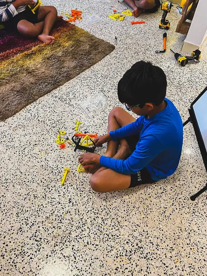 A young tinkerer sits on the floor, completely focused on assembling his project. My workshops are designed to be comfortable, hands-on spaces where kids can get lost in the process of building.