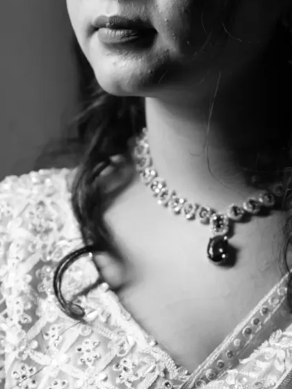 A close up black and white shot focusing on the bride's necklace and the intricate details of her embroidered blouse.